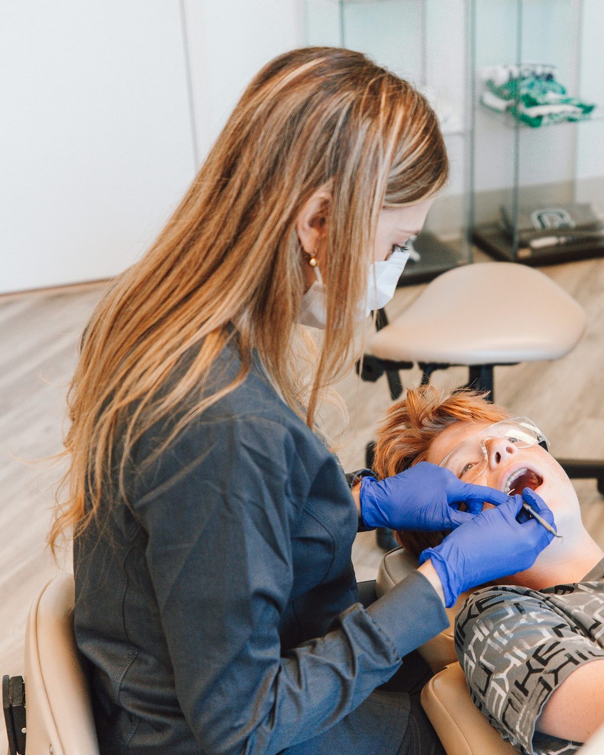 Een tandarts met mondmasker en blauwe handschoenen kijkt de tanden na van een jongen in de stoel