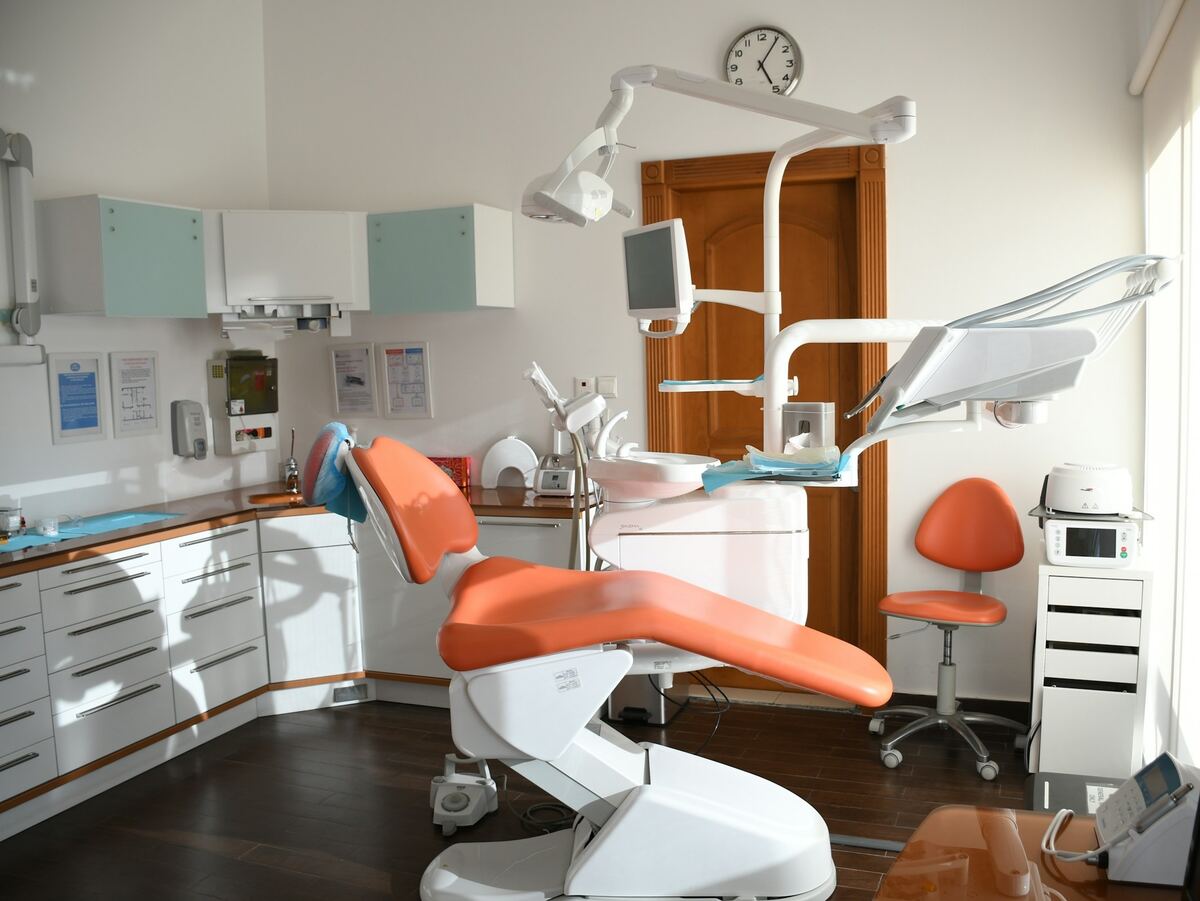 Lichte behandelkamer met een oranje tandartsstoel, een lamp en witte kasten